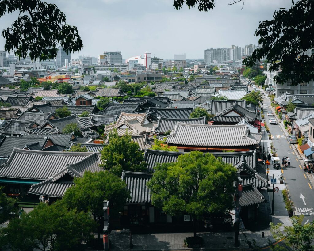 Aerial view of traditional rooftops in Jeonju Hanok Village, South Korea with city skyline in the background.