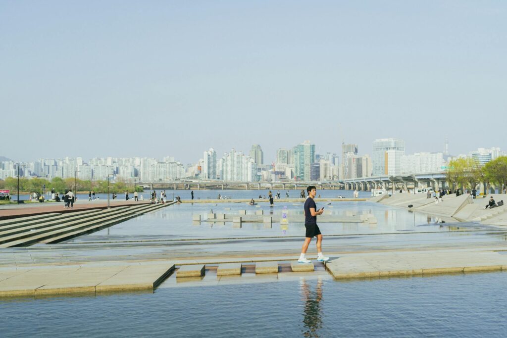 Someone walking the waterside path at a Han River park, apartments across the water